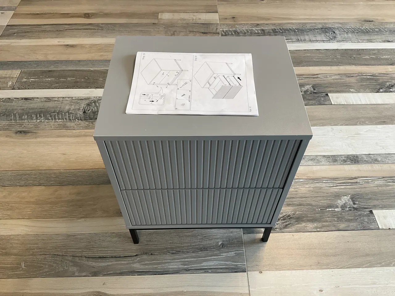 After: grey bedside cabinet assembled, the instructions lying on top